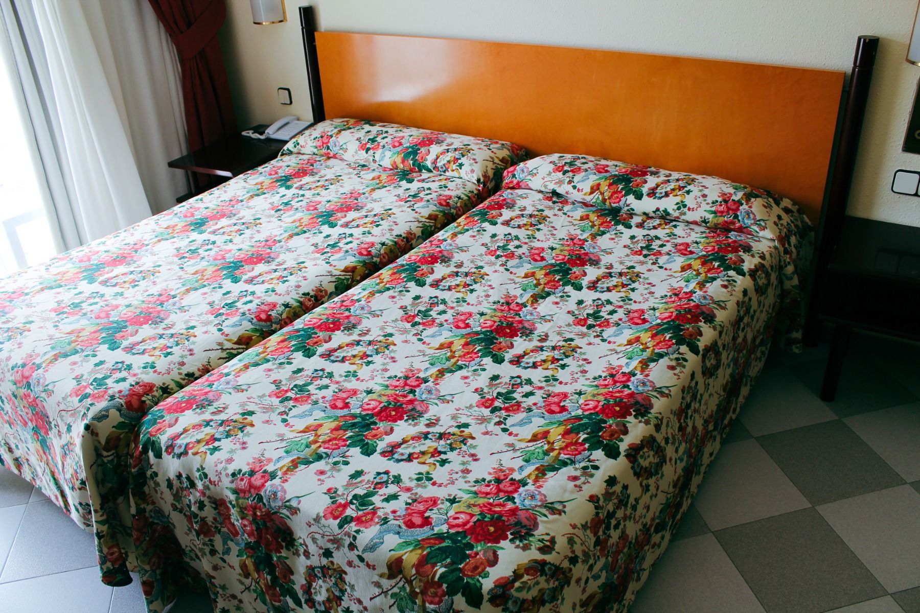 Nahaufnahme eines Doppelbetts im Hotelzimmer mit floralem Muster und hellem Kopfteil.