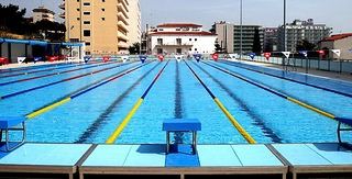 Außenansicht eines modernen Freibades mit mehreren Schwimmbahnen und Startblöcken, umgeben von städtischen Gebäuden.