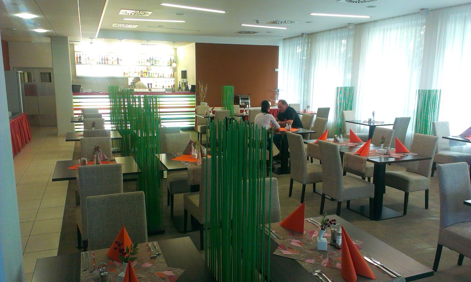 Helles Restaurant mit dekorativen grünen Elementen und gedeckten Tischen für Gäste.