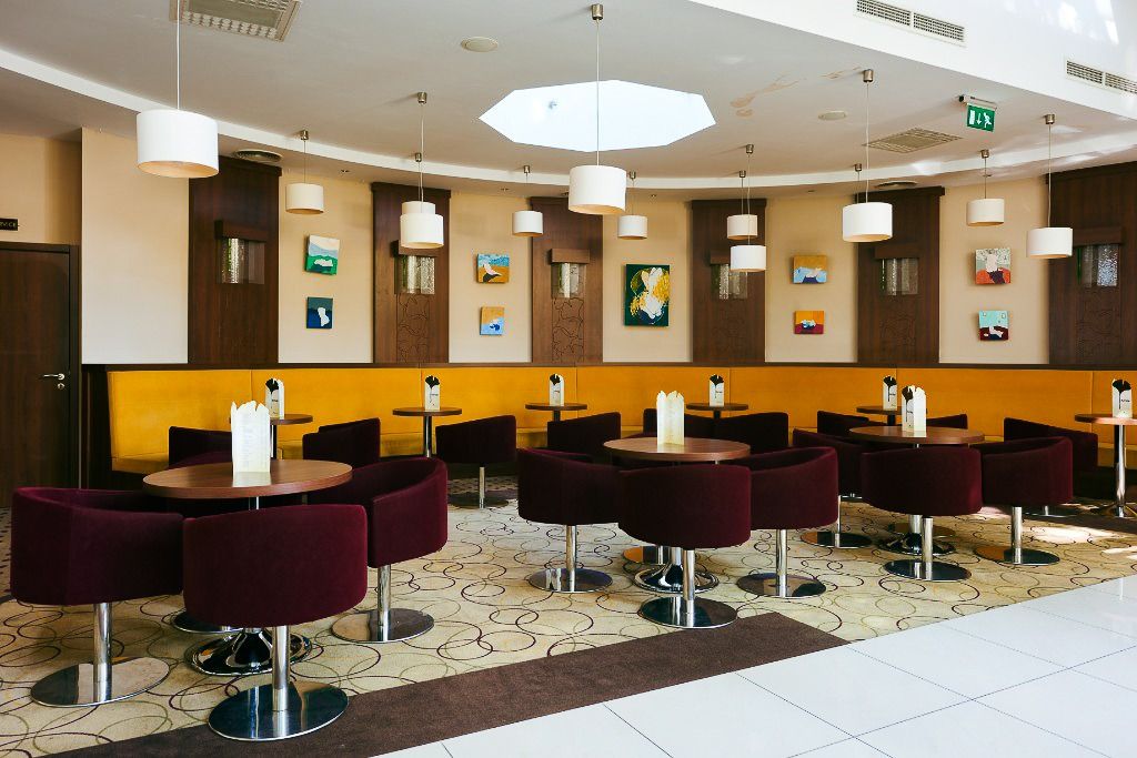 Eleganter Sitzbereich im Hotel Gingko mit runden Tischen, weinroten Sesseln und künstlerischer Wanddekoration.