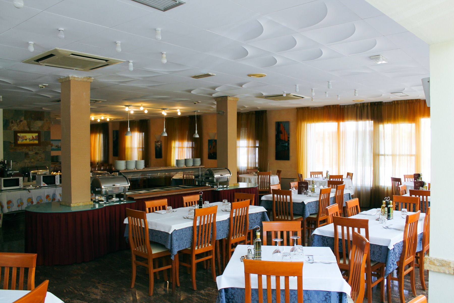 Geräumiger Speisesaal mit Buffetbereich, gedeckten Tischen, Holzstühlen und warmem Licht
