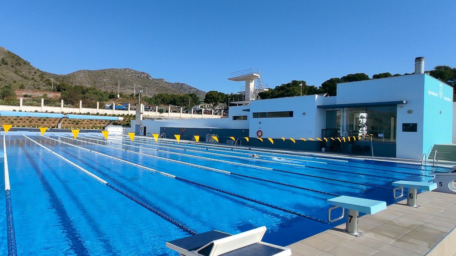 Freiluft-Schwimmbecken mit Startblöcken und Berglandschaft im Hintergrund.