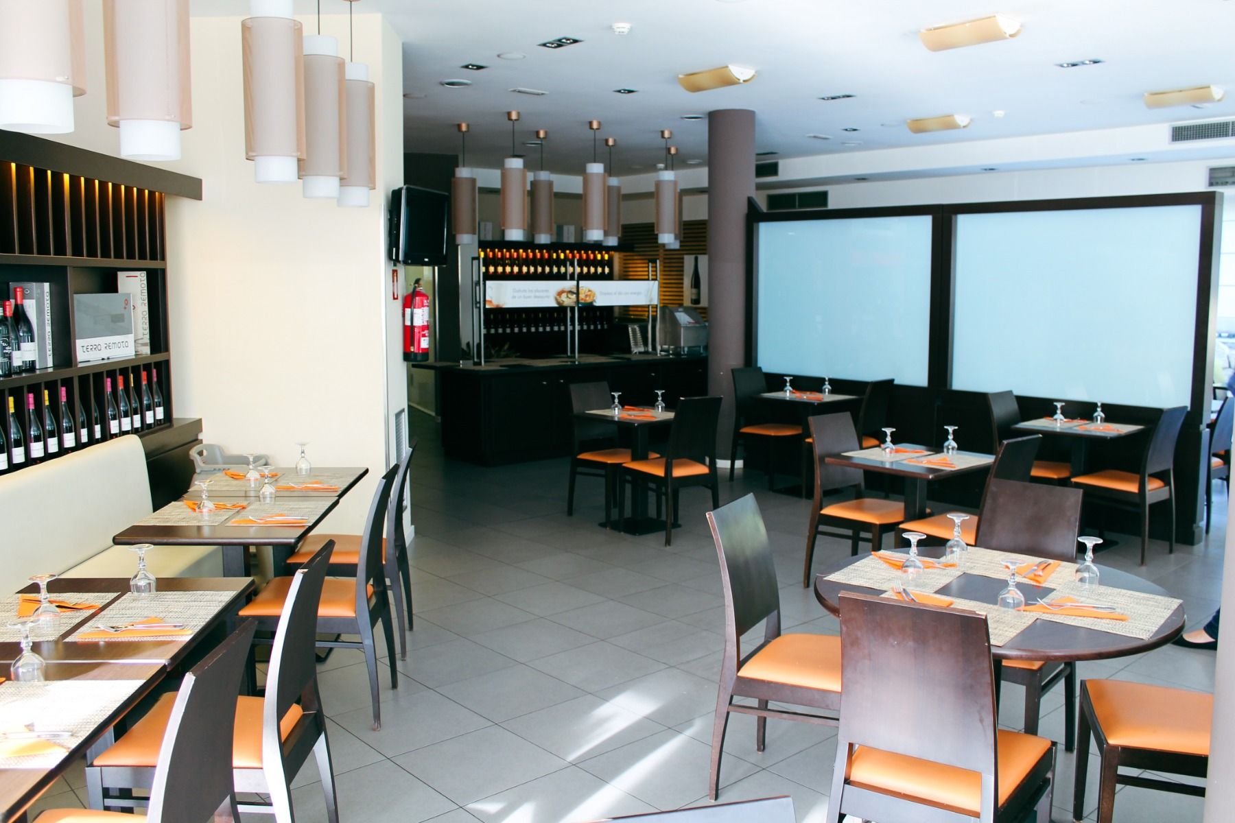 Hotelrestaurant mit dunklen Holztischen, orangefarbenen Stühlen und stilvollen Lampen. Die Tische sind gedeckt, und ein Weinschrank befindet sich im Hintergrund.