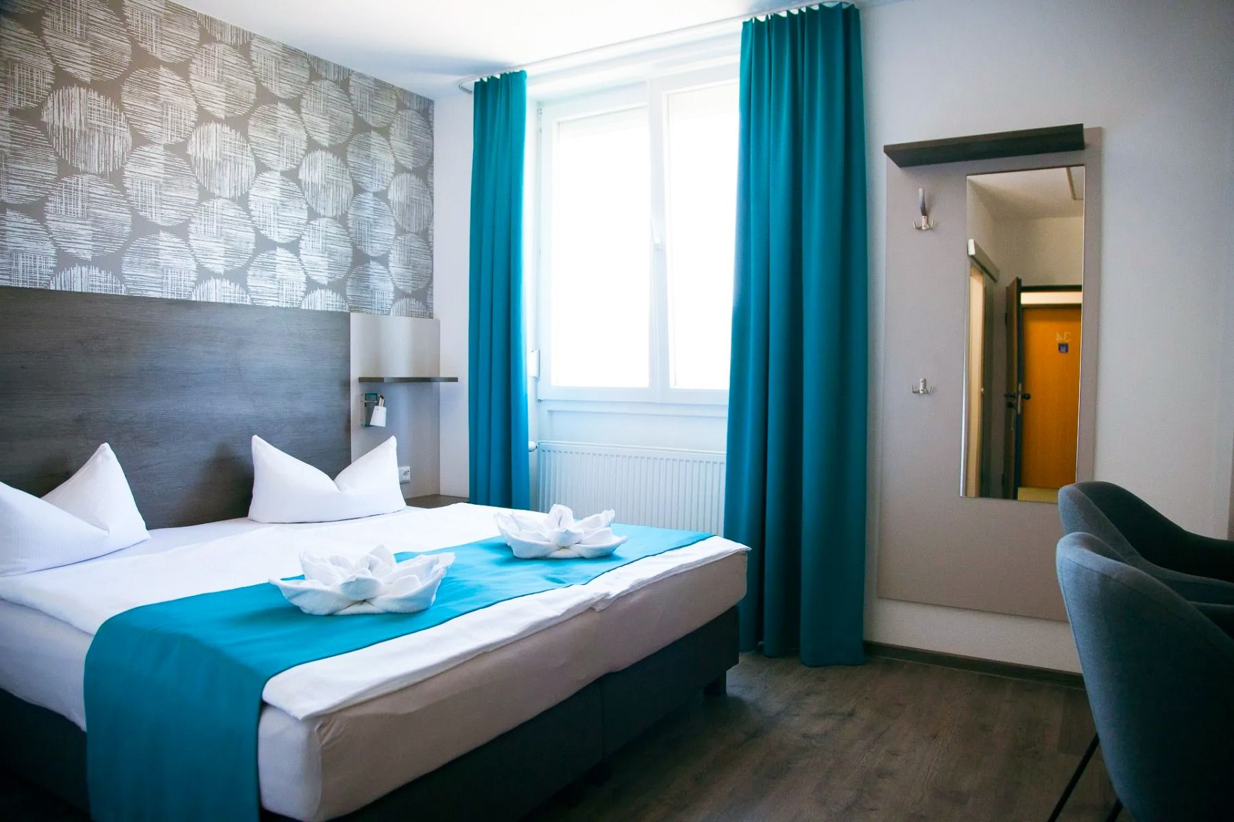 Doppelzimmer im Hotel im Kaiserpark mit großem Bett, Fenster, Spiegelgarderobe und Tisch mit Stühlen