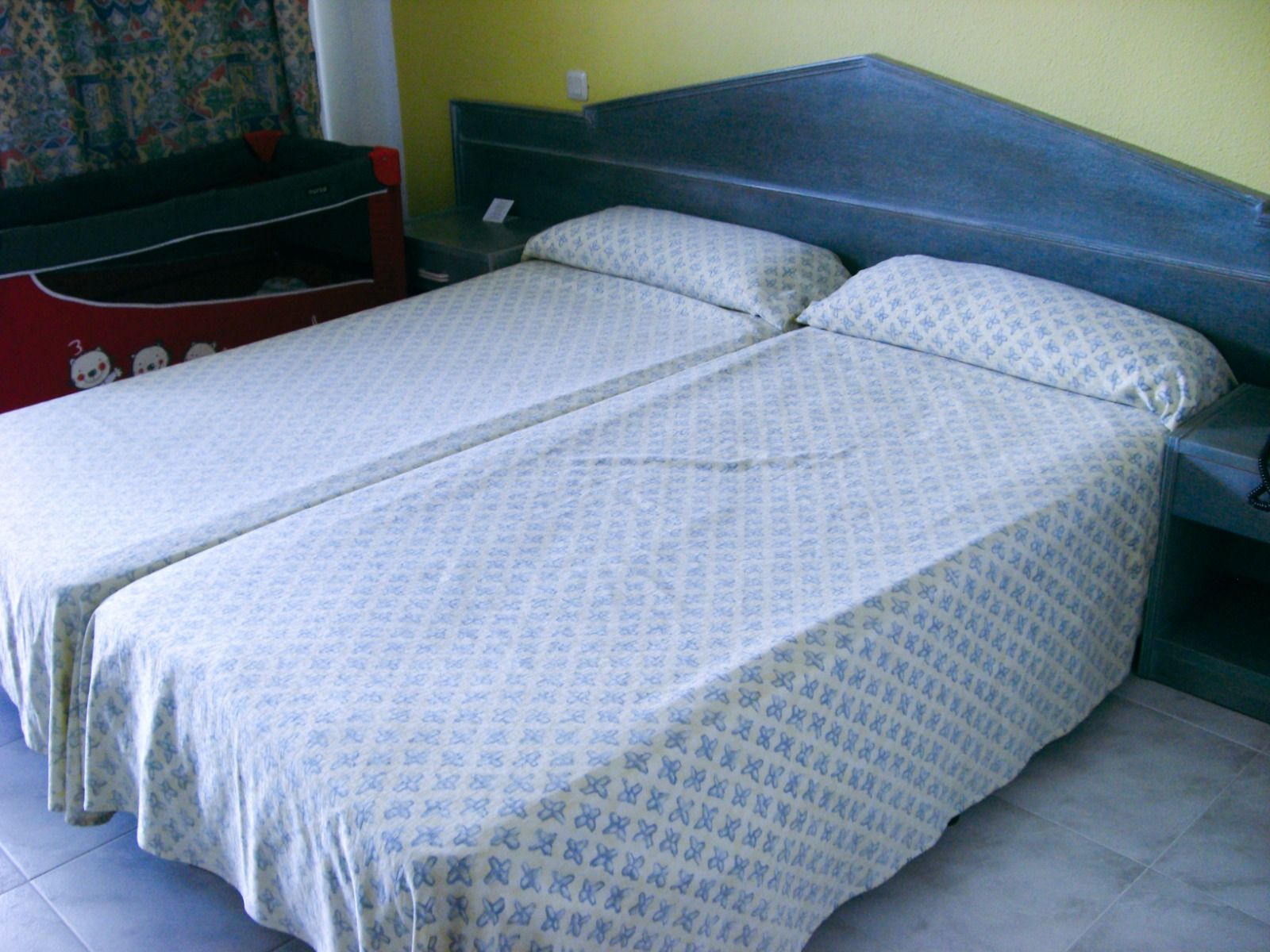 Einfach eingerichtetes Hotelzimmer mit einem Doppelbett, gelber Wand und minimalistischer Ausstattung.
