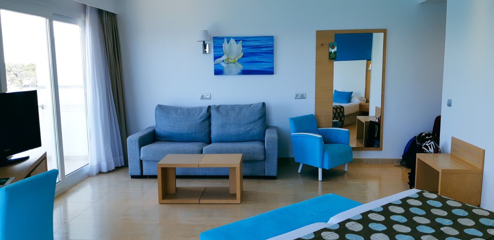Hotelzimmer mit gemütlicher Sitzecke, Sofa und Sesseln in Blautönen, sowie einem großen Fenster mit viel Tageslicht.