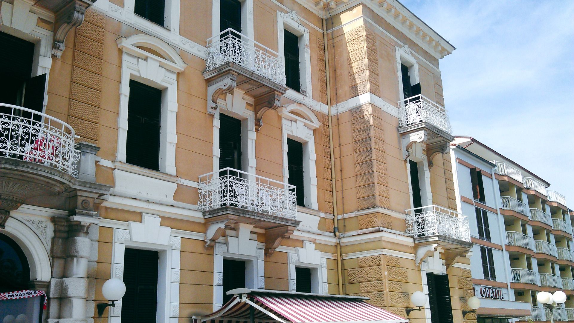 Historische Gebäudeansicht des Hotels Opatija mit dekorativen Balkonen und weißen Fenstern auf gelber Außenfassade