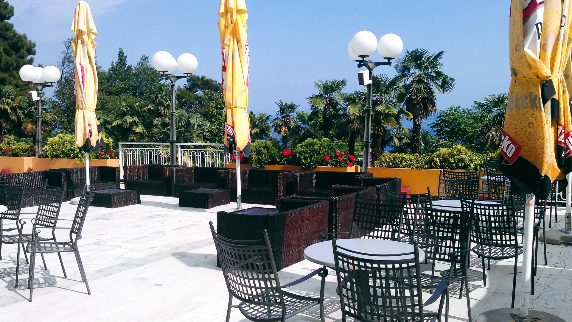 Eine gemütliche Terrasse mit modernen Sitzmöbeln, umgeben von Palmen und Sonnenschirmen, mit Blick auf die Umgebung und das Meer
