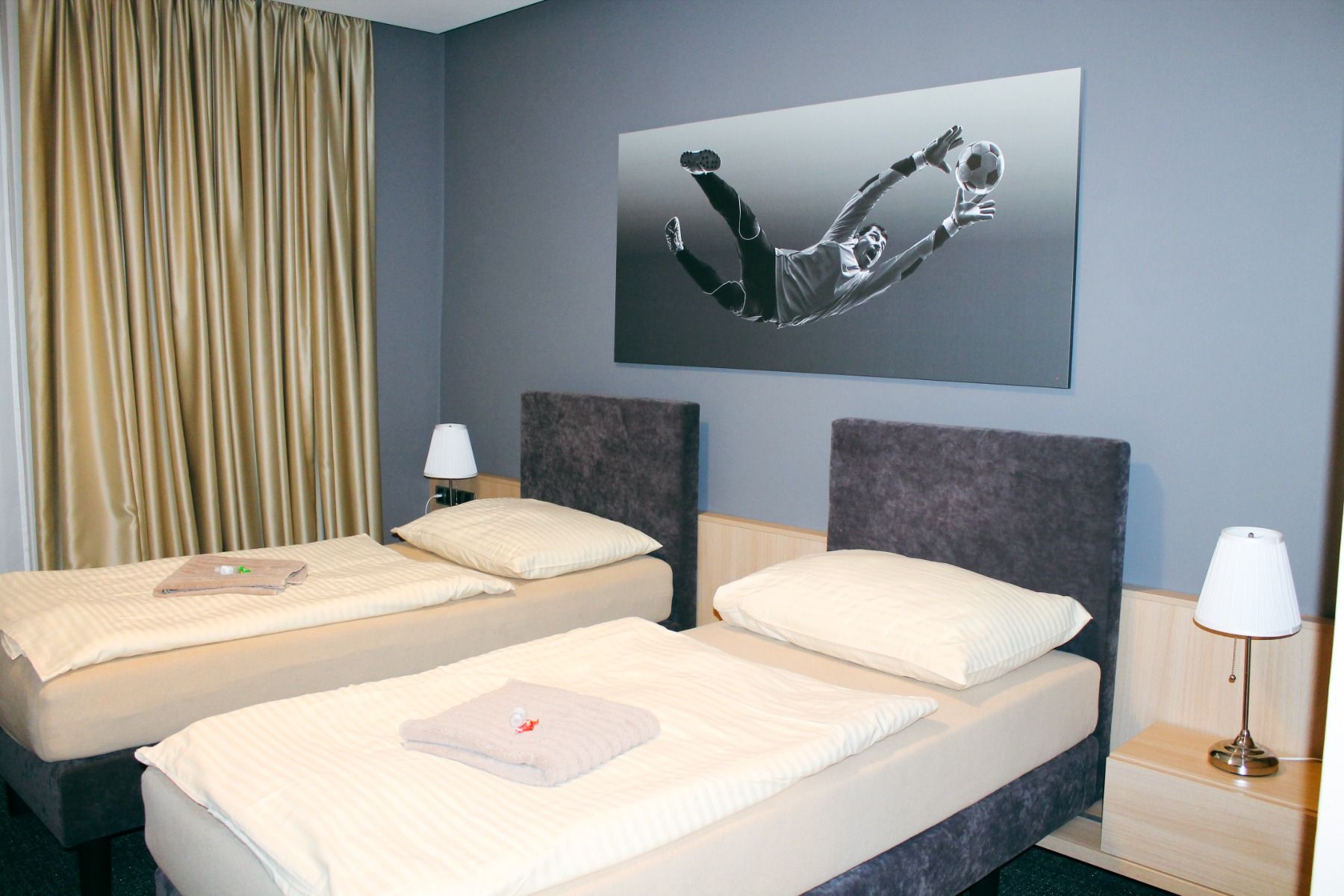 Modern eingerichtetes Doppelzimmer mit zwei Einzelbetten und einem Wandbild eines Torwarts.