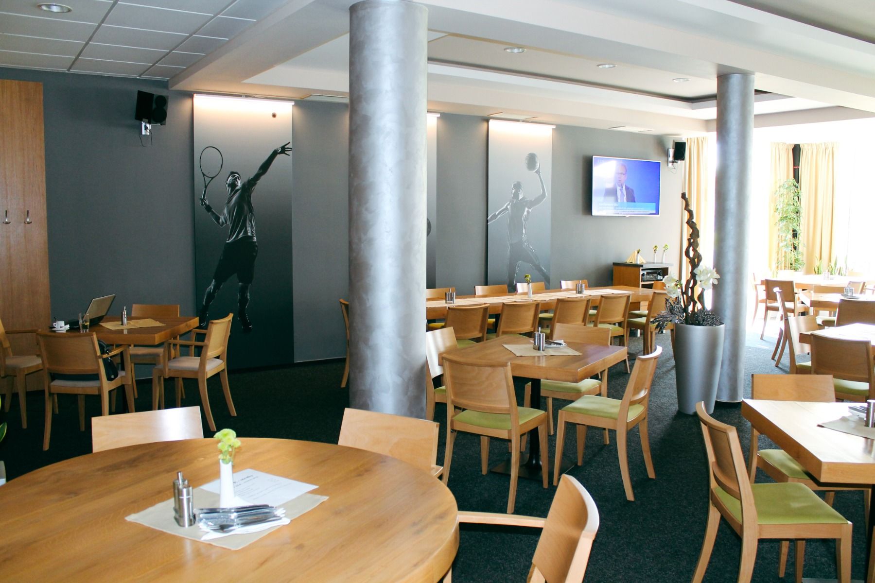 Restaurantbereich mit Sportmotiven an den Wänden und Holzstühlen.