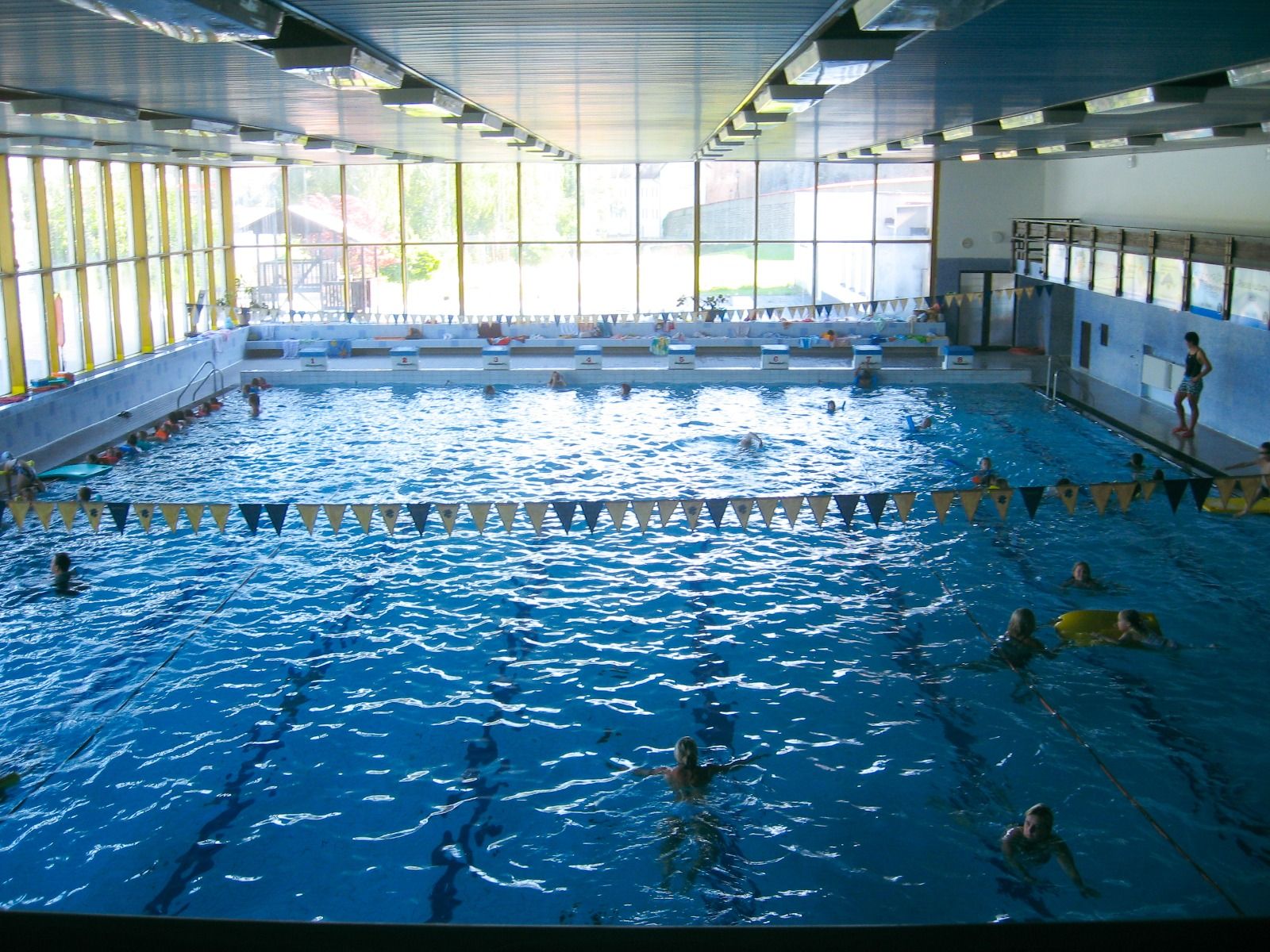 Innenansicht eines Schwimmbads mit mehreren Bahnen und schwimmenden Gästen.