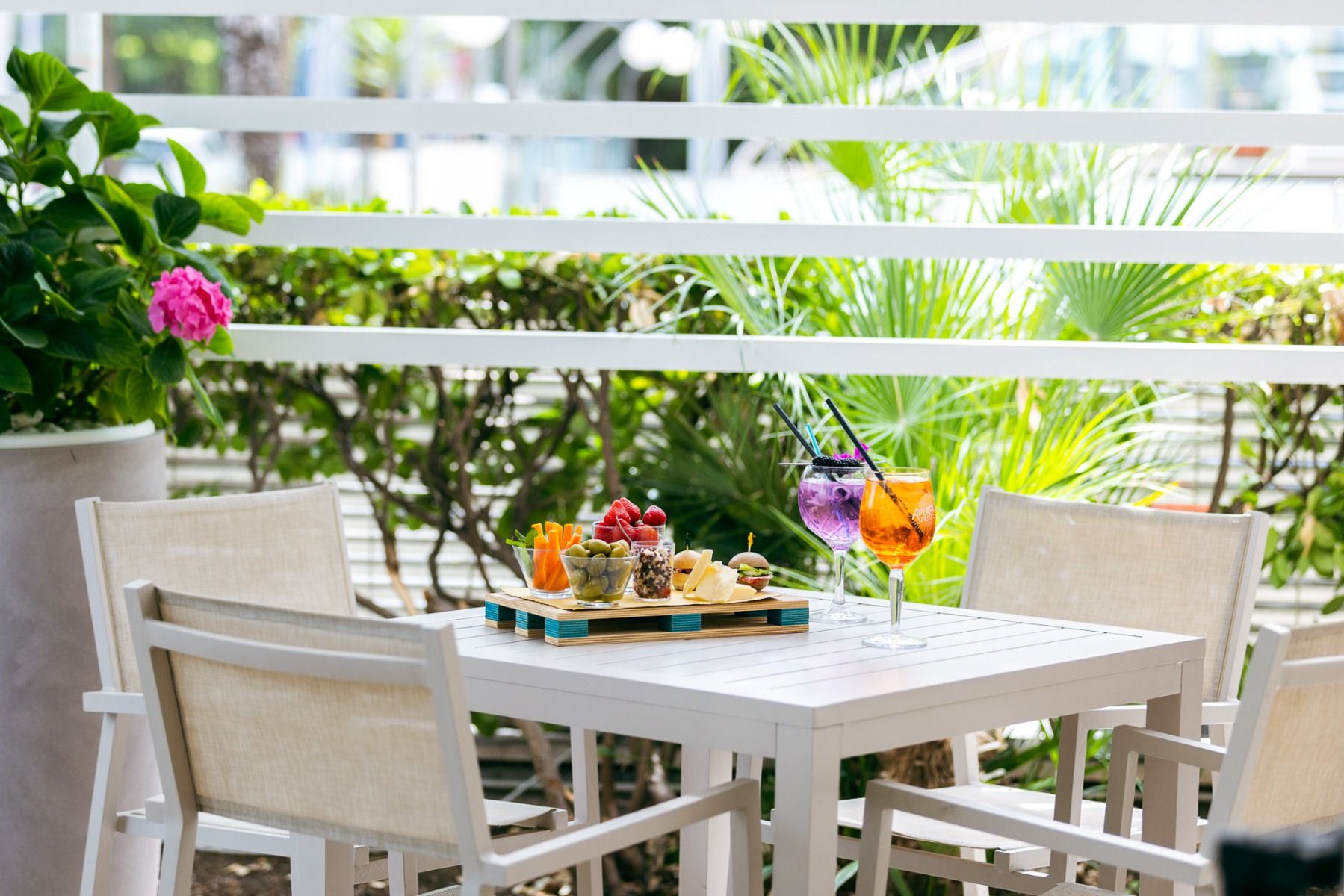 Sonnige Veranda im Hotel Poker in Riccione, Italien, mit Tisch, Snacks, Drinks und Pflanzen im Hintergrund
