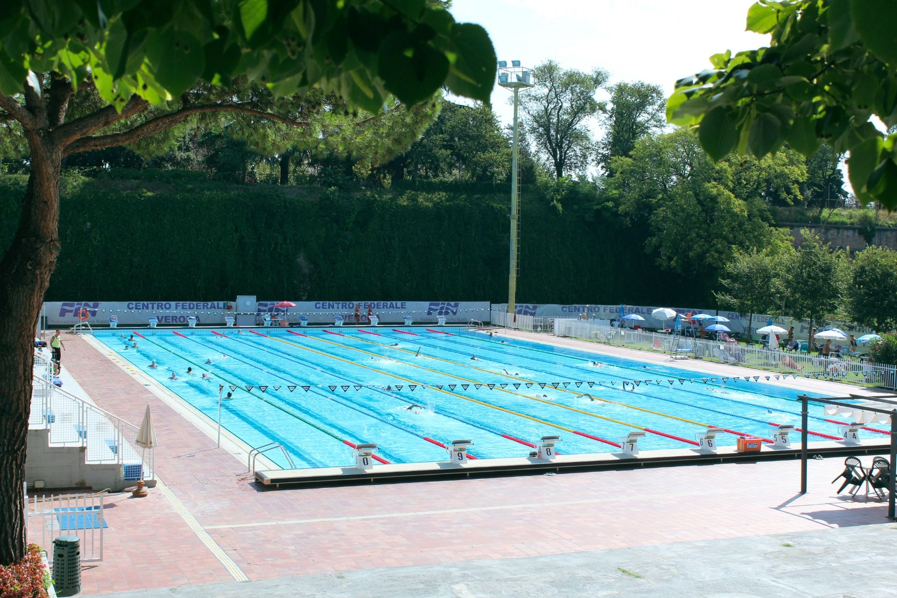 Außenpool mit mehreren Schwimmbahnen, umgeben von grünen Bäumen und Sonnenschirmen, ideal für Wettkämpfe und Training
