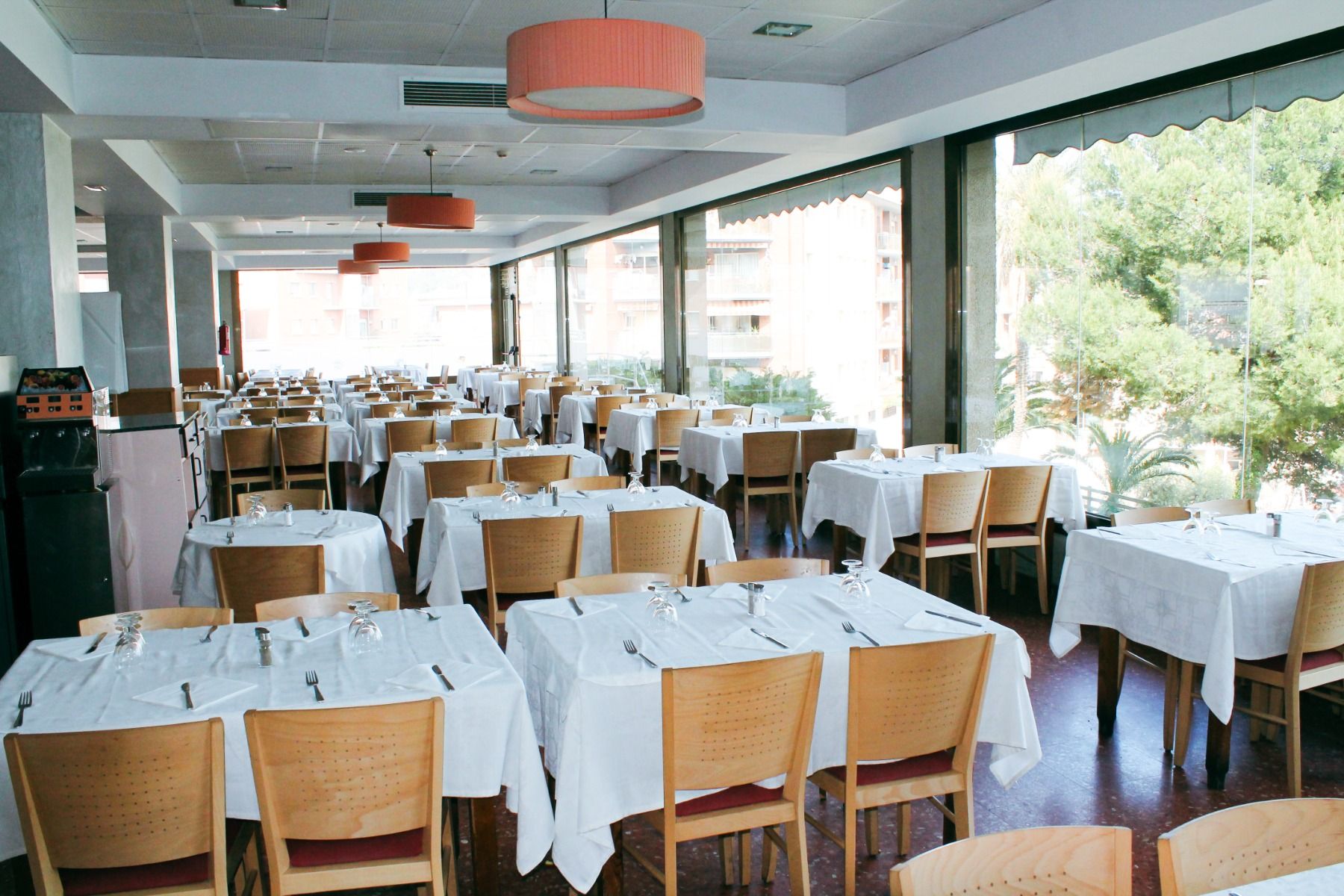 Helles Hotelrestaurant mit bodentiefen Fenstern, weißen Tischdecken und gedeckten Tischen für Gäste.