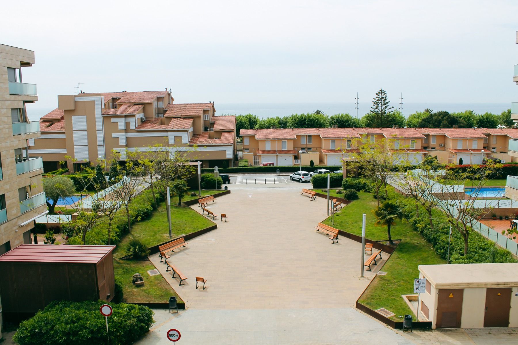 Weitläufige Hotelanlage des Hotels Sant Jordi mit gepflegtem Garten, Sitzbänken und Blick auf das Meer im Hintergrund.