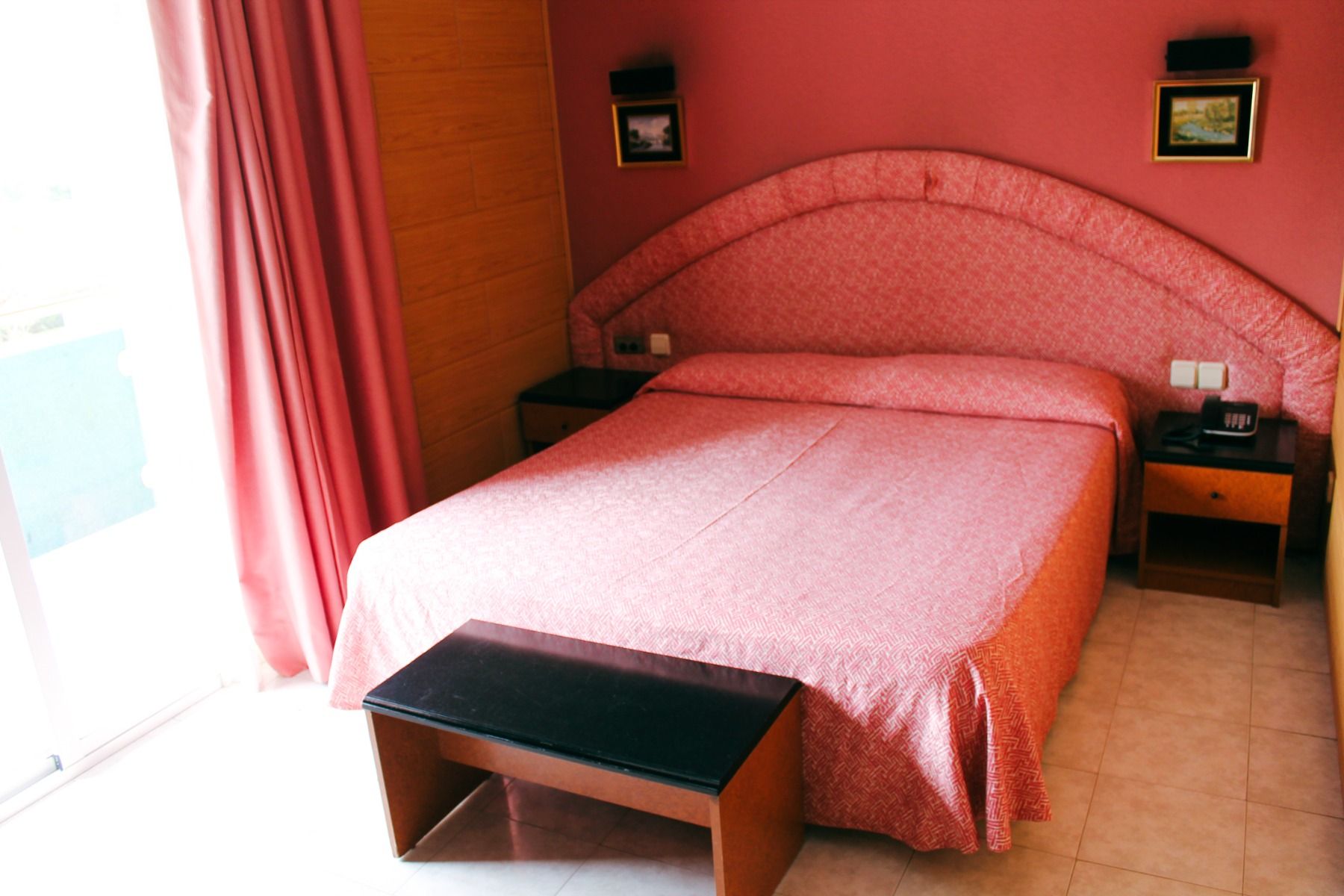 Gemütliches Hotelzimmer mit einem großen Doppelbett, rosa Einrichtung und natürlichem Licht durch ein Fenster.