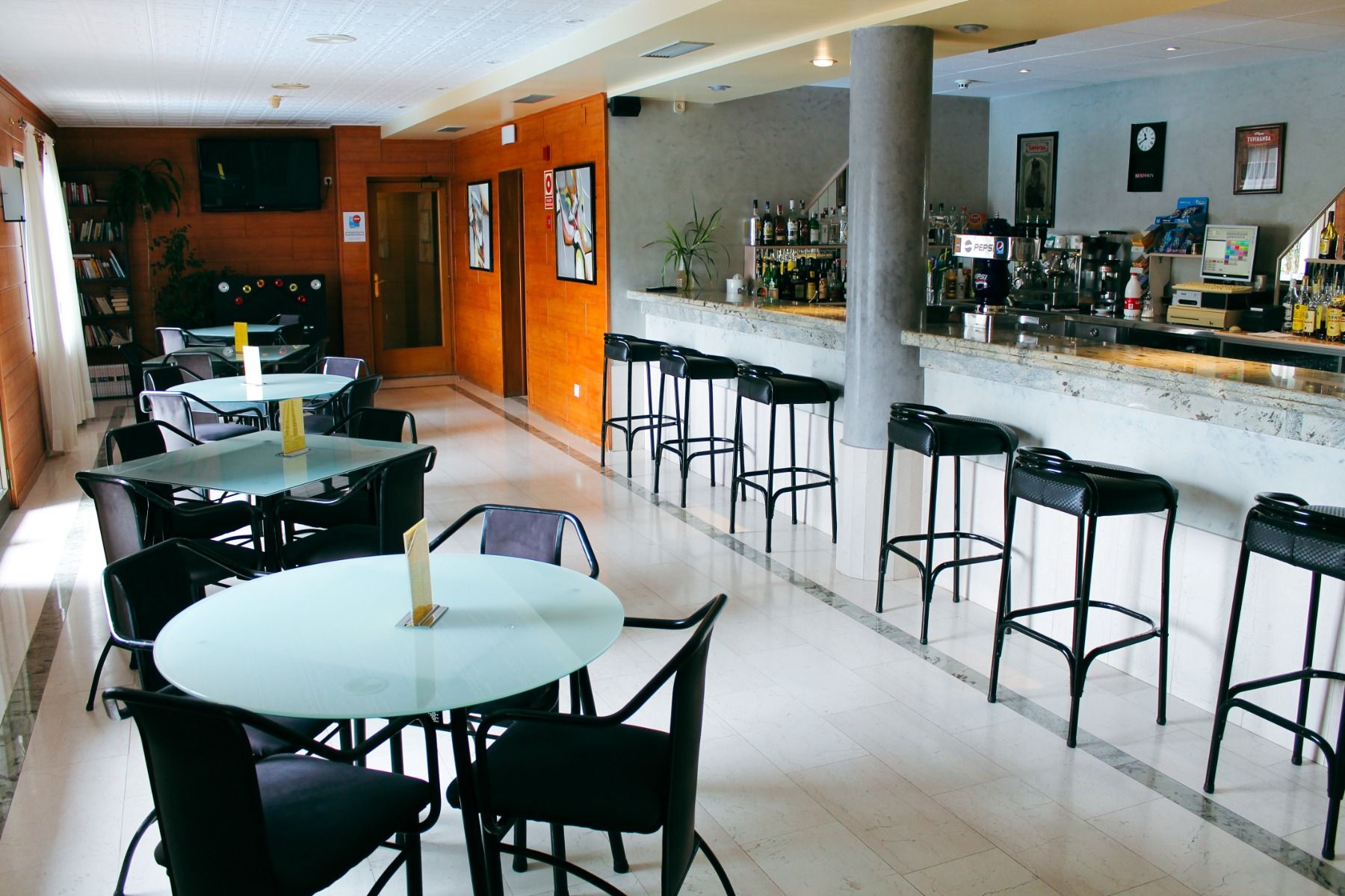 Moderne Hotelbar mit Marmortheke, Barhockern und Glasrundtischen, gemütliche Atmosphäre für Gäste.