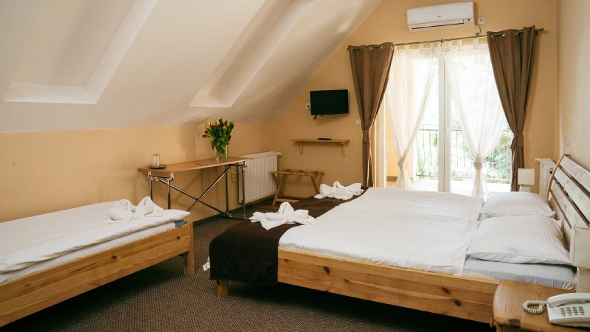 Gemütliches Zimmer mit Holzbetten, heller Einrichtung und Fenstern mit Vorhängen, die Zugang zu einem Balkon bieten.