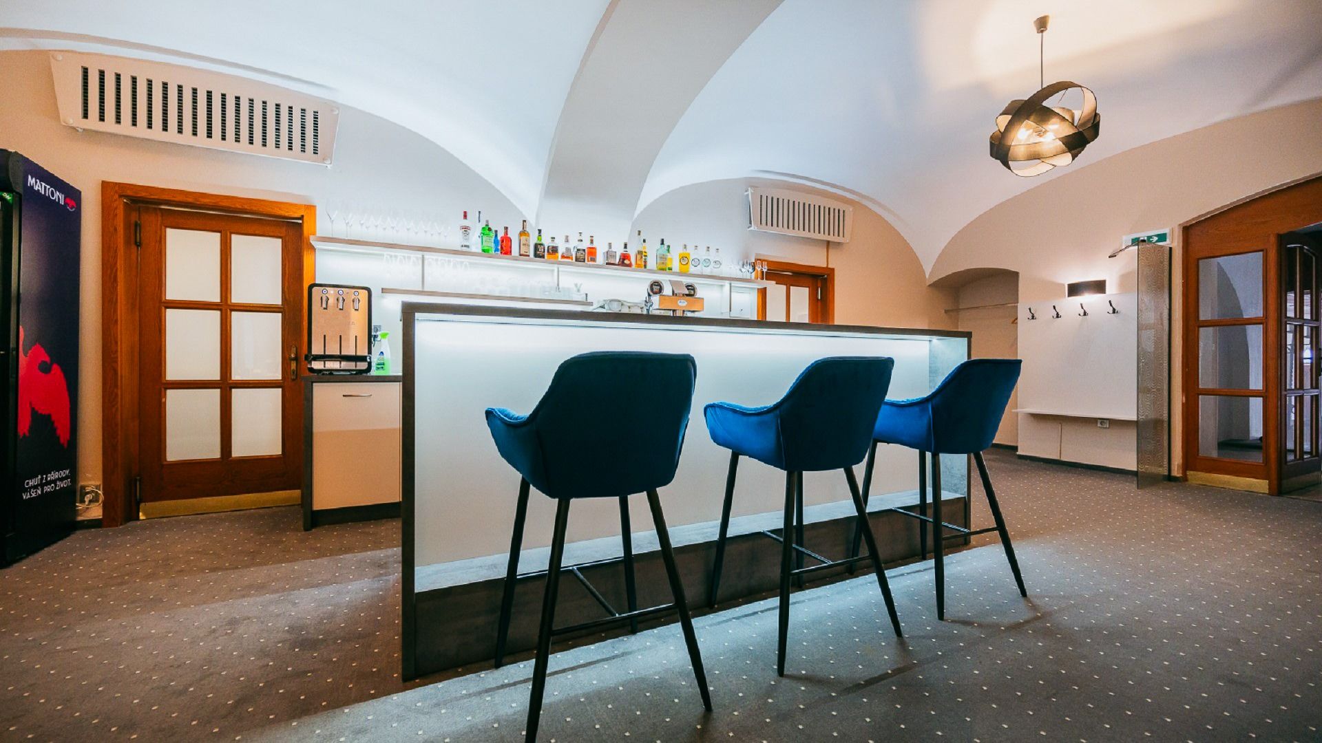 Moderne Hotelbar mit beleuchtetem Tresen, blauen Barhockern und gewölbter Decke.
