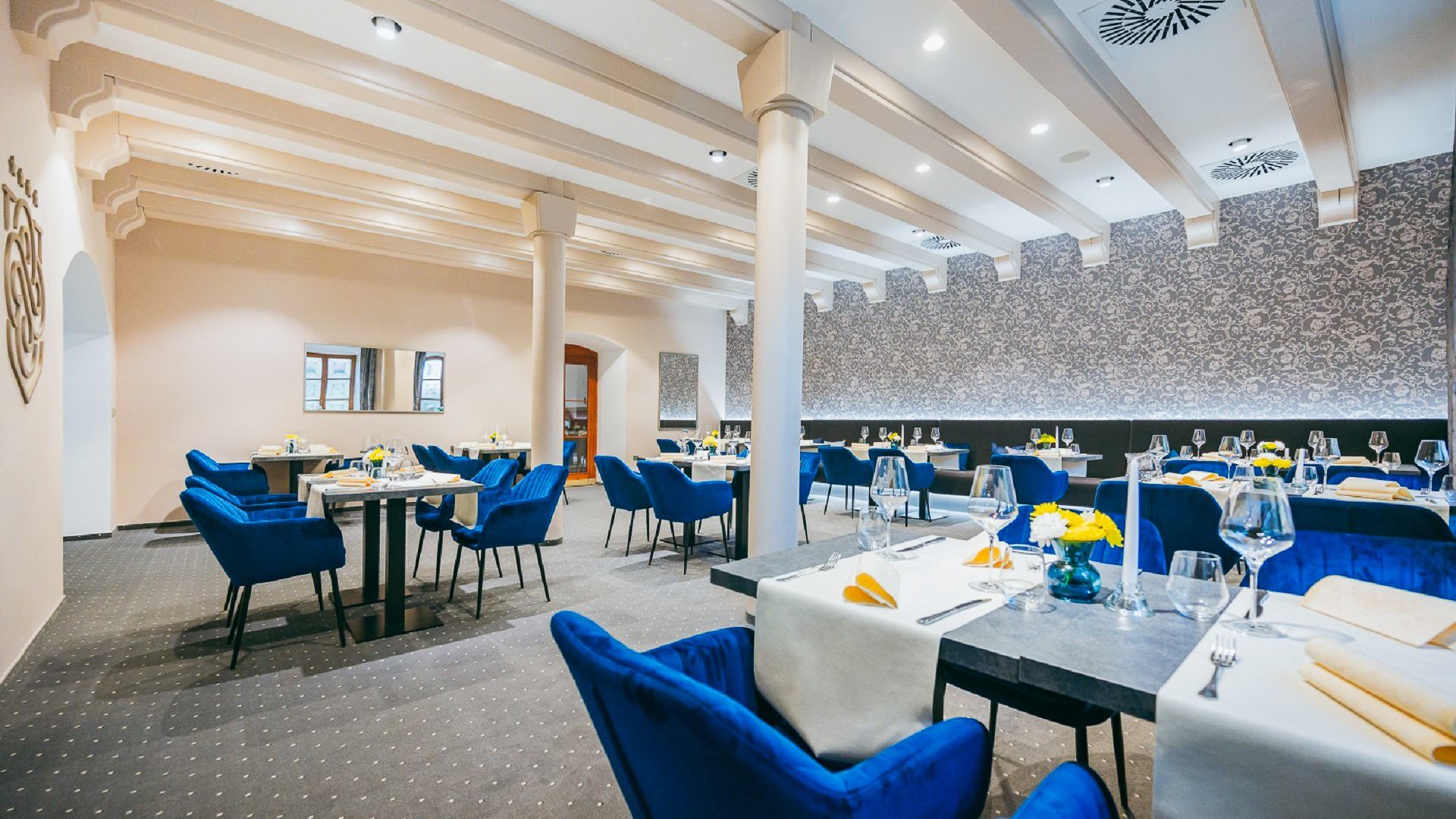 Elegantes Hotelrestaurant mit blauen Polsterstühlen, gedeckten Tischen und stilvoller Beleuchtung.