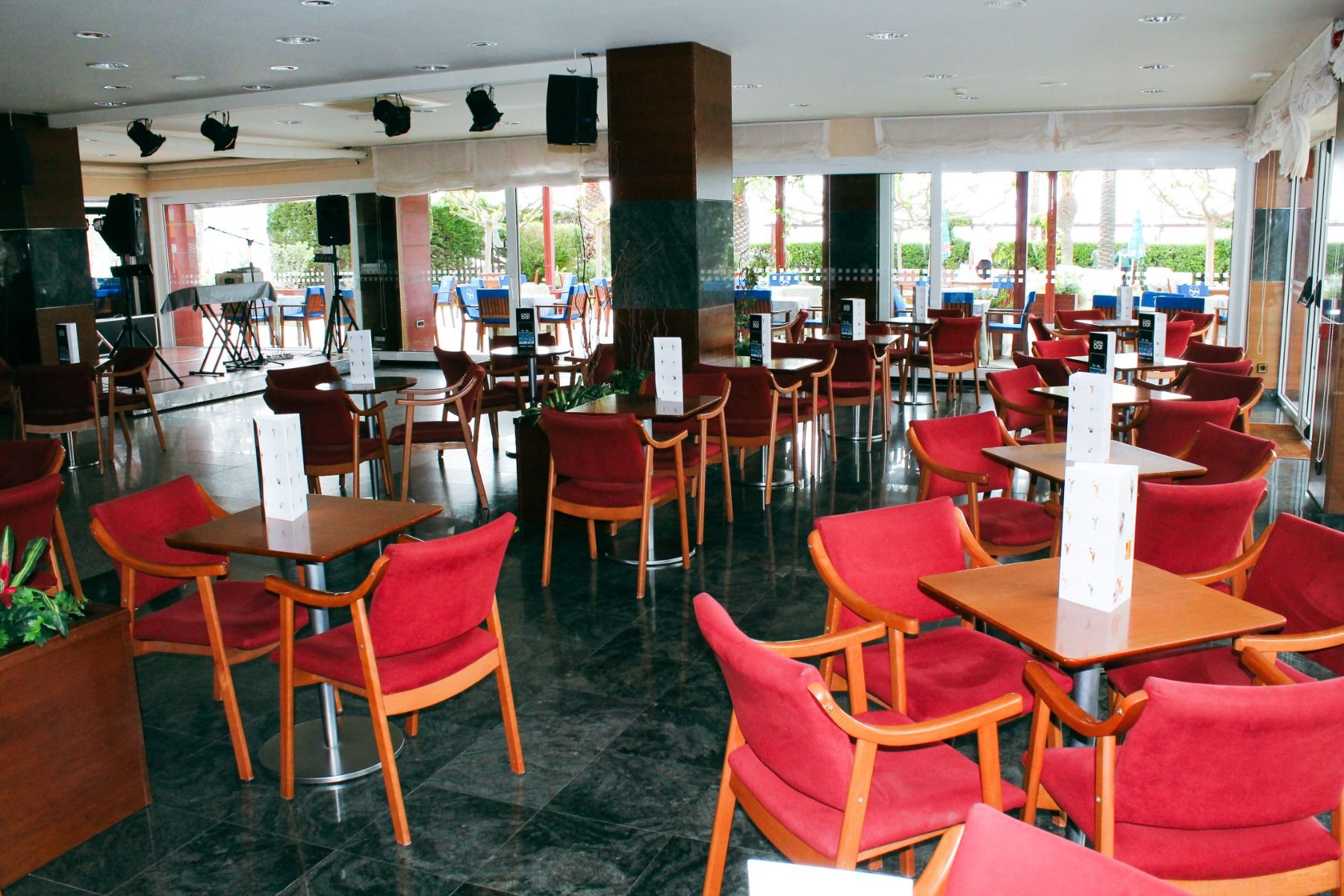 Elegante Hotelbar mit roten Sesseln, Holztischen und einer Bühne für Live-Unterhaltung, perfekt für gesellige Abende.