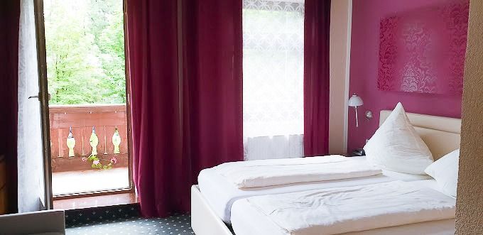 Doppelzimmer mit Zugang zum Balkon und lila Wänden und Vorhängen im Kastenauer Hof