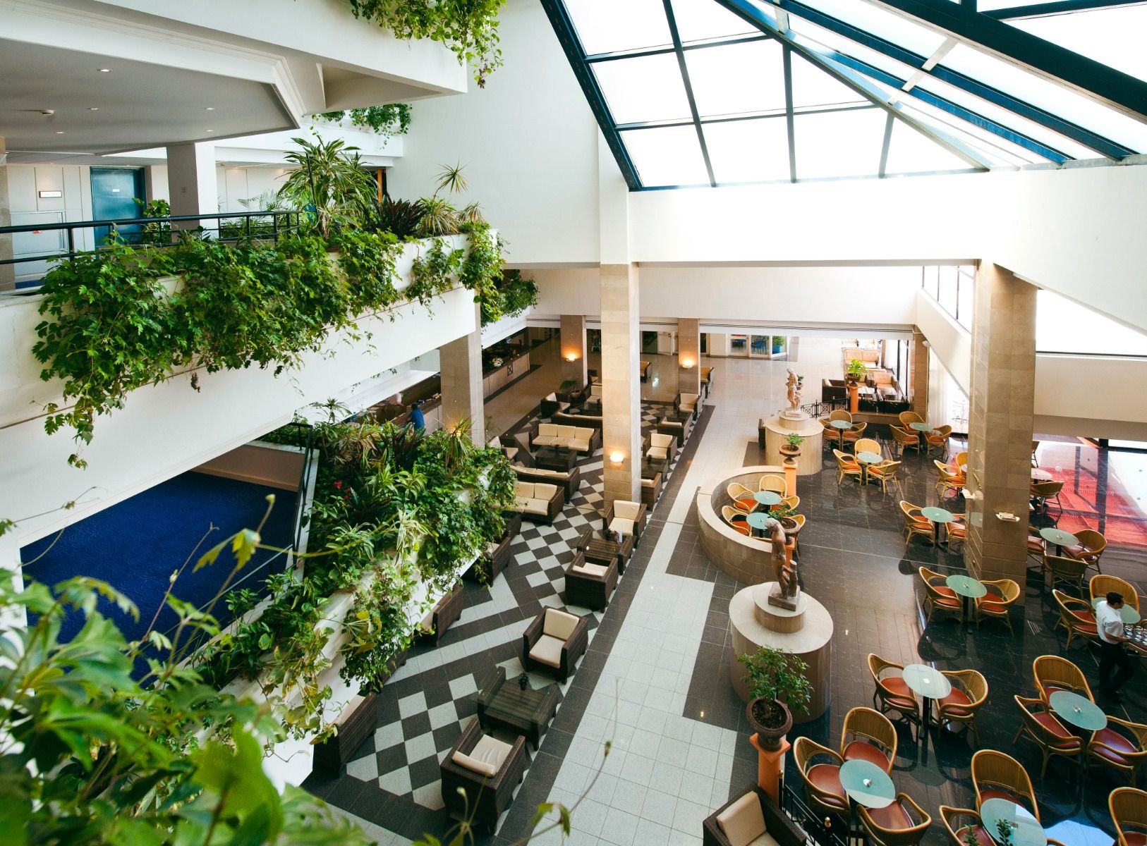 Großzügiges, lichtdurchflutetes Hotel-Atrium mit viel Grünpflanzen, Sitzbereichen und Café im Louis Phaethon Beach Hotel.