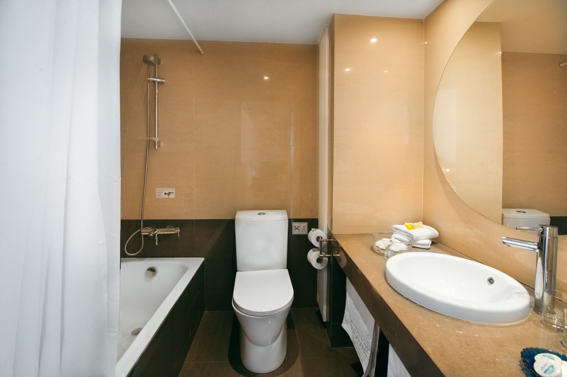 Modernes Badezimmer im Louis Phaethon Beach Hotel mit Badewanne, WC und Waschbecken in Beige- und Brauntönen.