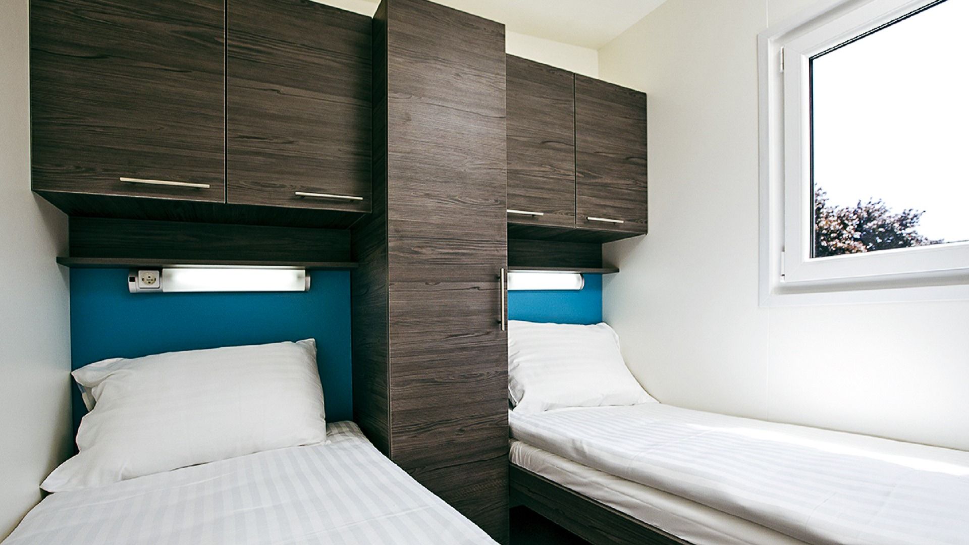 Schlafzimmer mit zwei Einzelbetten und blau akzentuierten Wänden in einem Mobilheim.