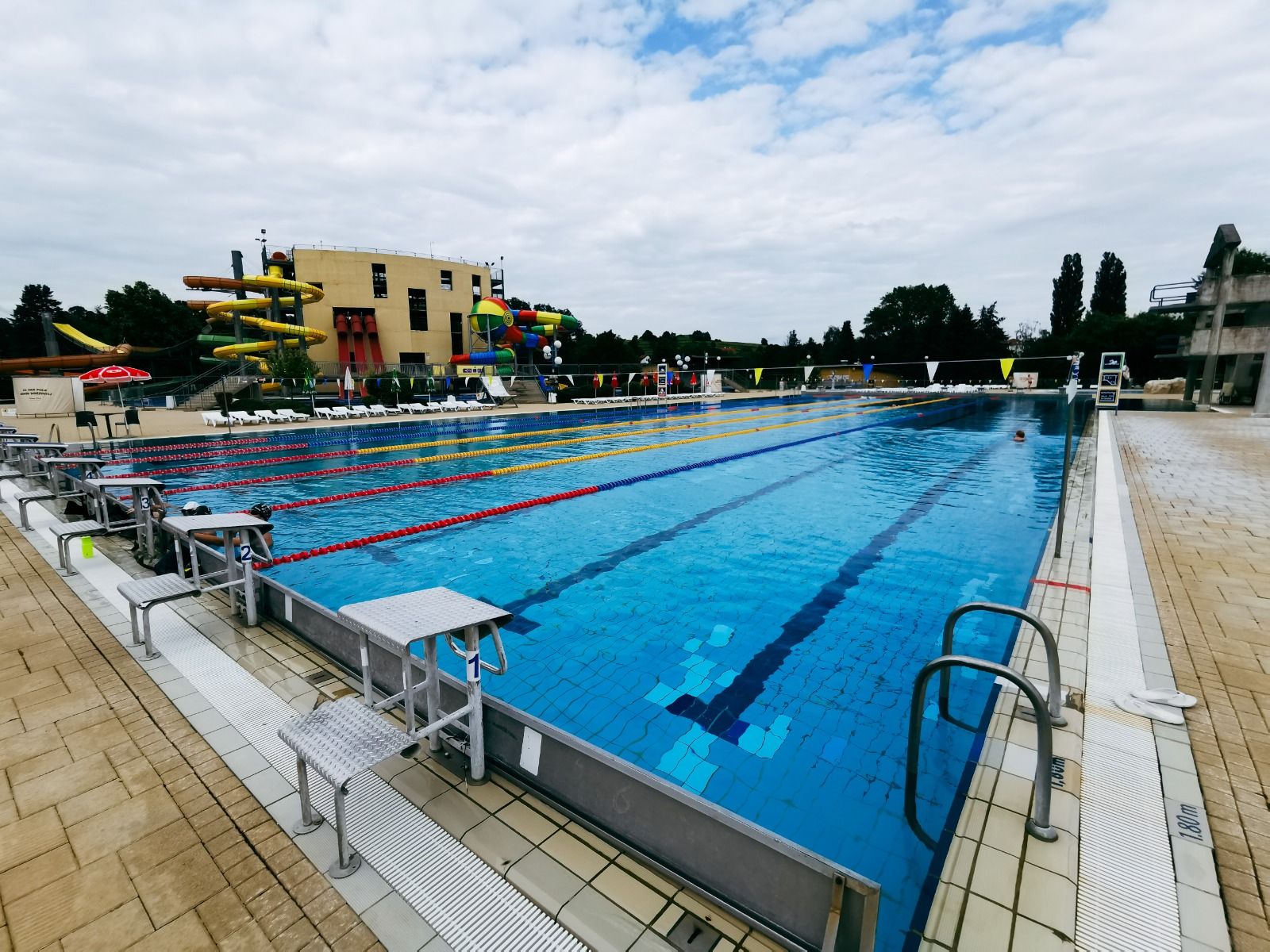 Schwimmbad mit farbigen Wasserrutschen, umgeben von Sonnenschirmen und Liegestühlen.