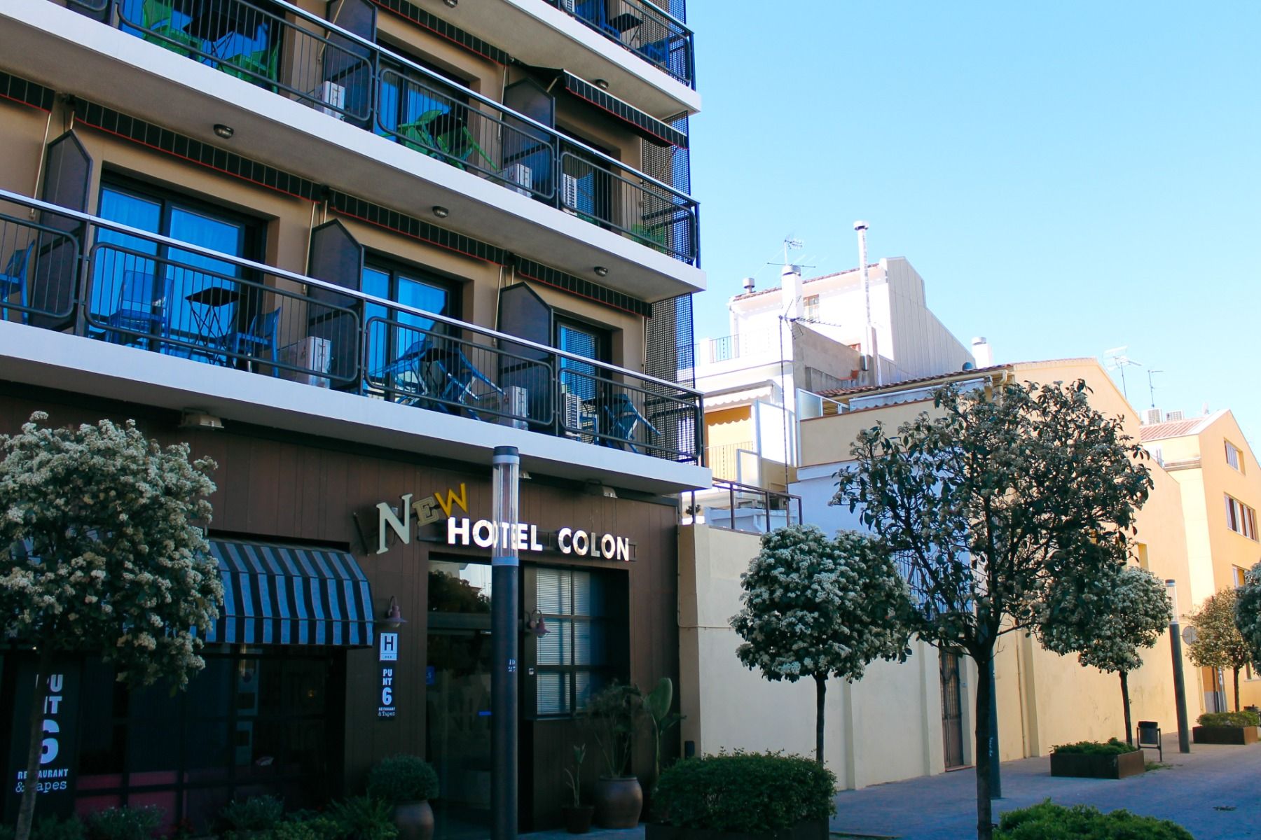 Das moderne New Hotel Colon mit mehreren Stockwerken, Balkonen und einer gepflegten Fassade, umgeben von grünen Bäumen und urbaner Architektur.