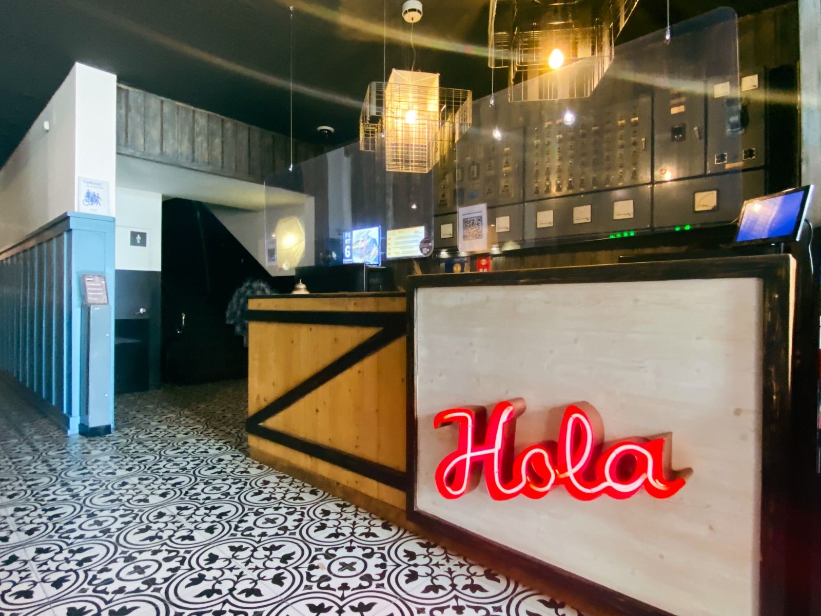 Der stilvolle Empfangsbereich des Hotels mit einer modernen Rezeption aus Holz, verziert mit einer neonroten „Hola“-Begrüßung.