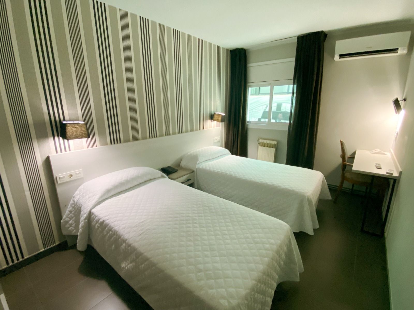 Ein modernes Doppelzimmer mit zwei Einzelbetten, weißer Bettwäsche und dekorativen Streifen an der Wand.