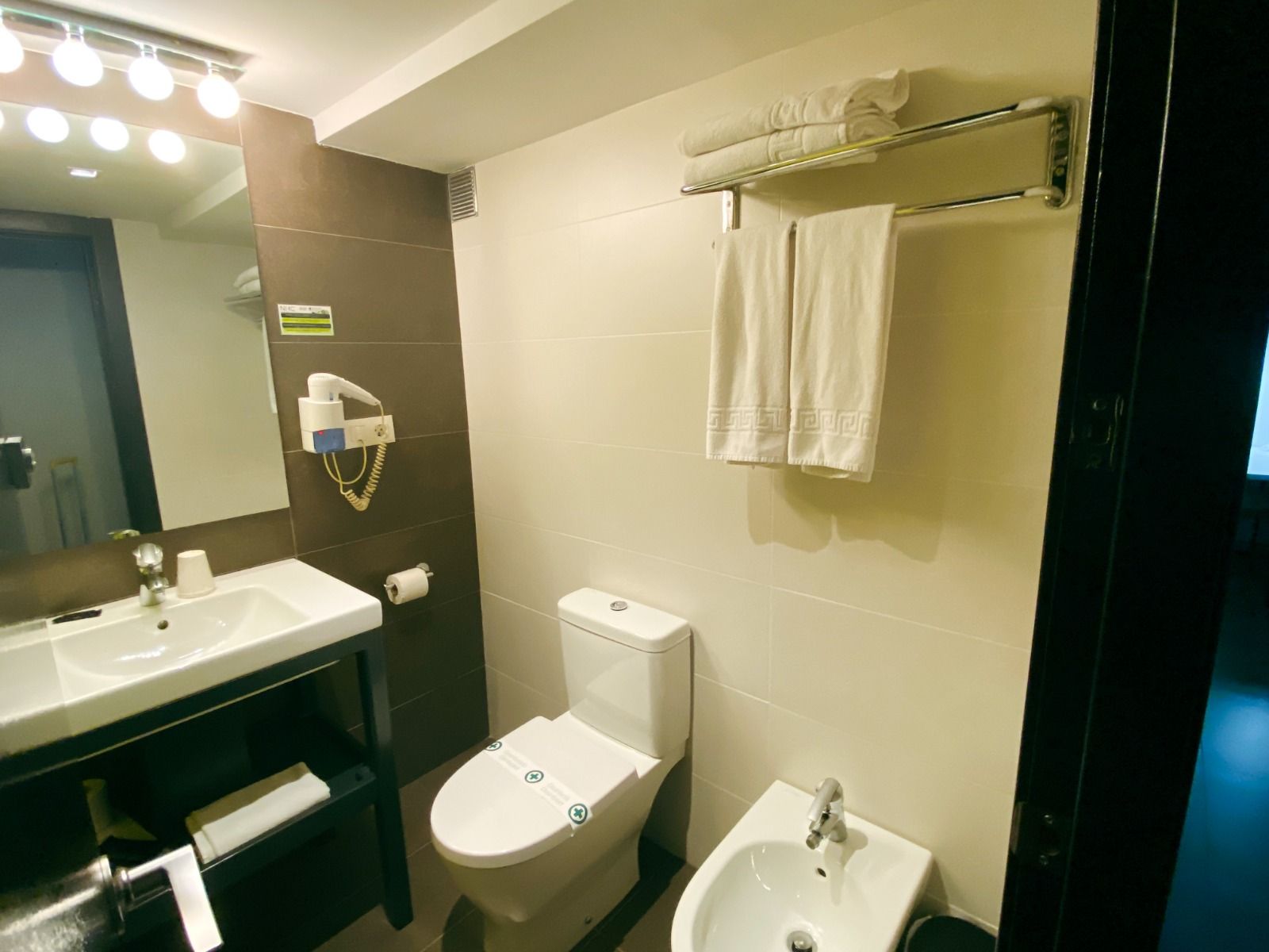 Ein sauberes und modern eingerichtetes Badezimmer mit Waschbecken, Toilette, Bidet und weißen Handtüchern.