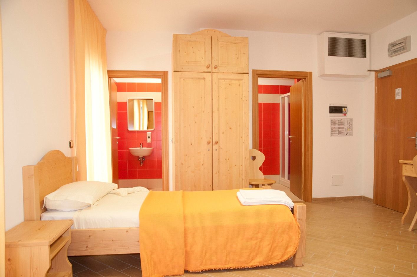 Zimmer mit Holzmöbeln, ein Bett steht im Vordergrund, dahinter ist der Zugang zum Bad mit roten Fliesen im Ostello Sportivo