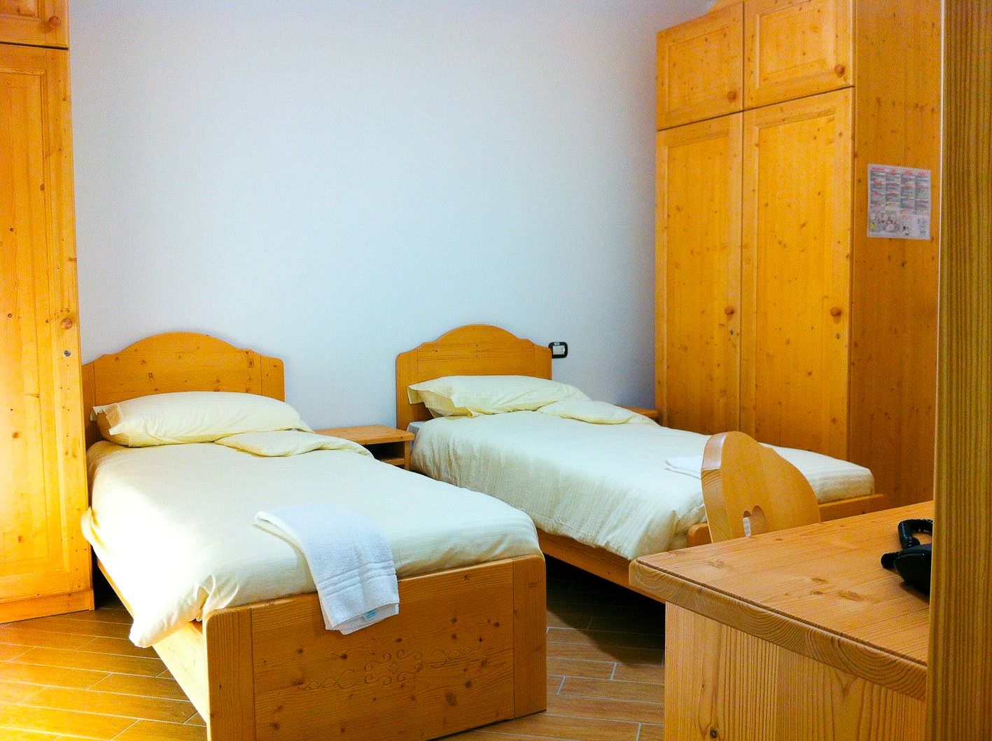 Einfach gehaltenes Doppelzimmer im Ostello Sportivo mit zwei Einzelbetten, sowie Schrank, Tisch und Stuhl jeweils aus Holz