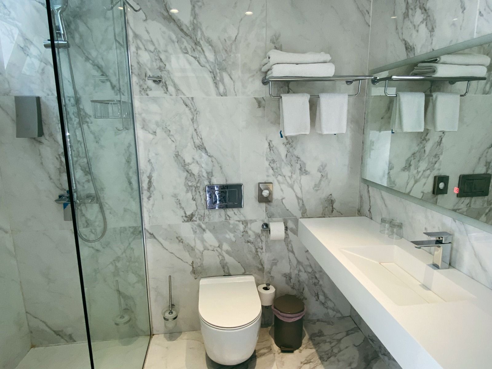 Modernes Badezimmer mit einer Dusche mit Glasfront und einer marmorierten Wand.