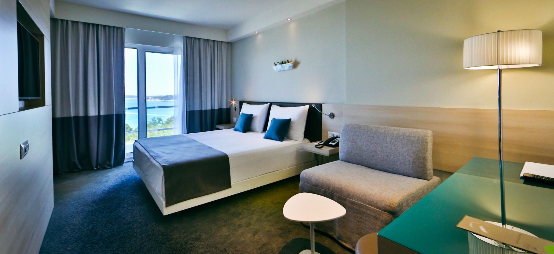 Helles Zimmer mit modernem Design, Doppelbett, Sitzbereich und großem Fenster mit Blick auf das Meer