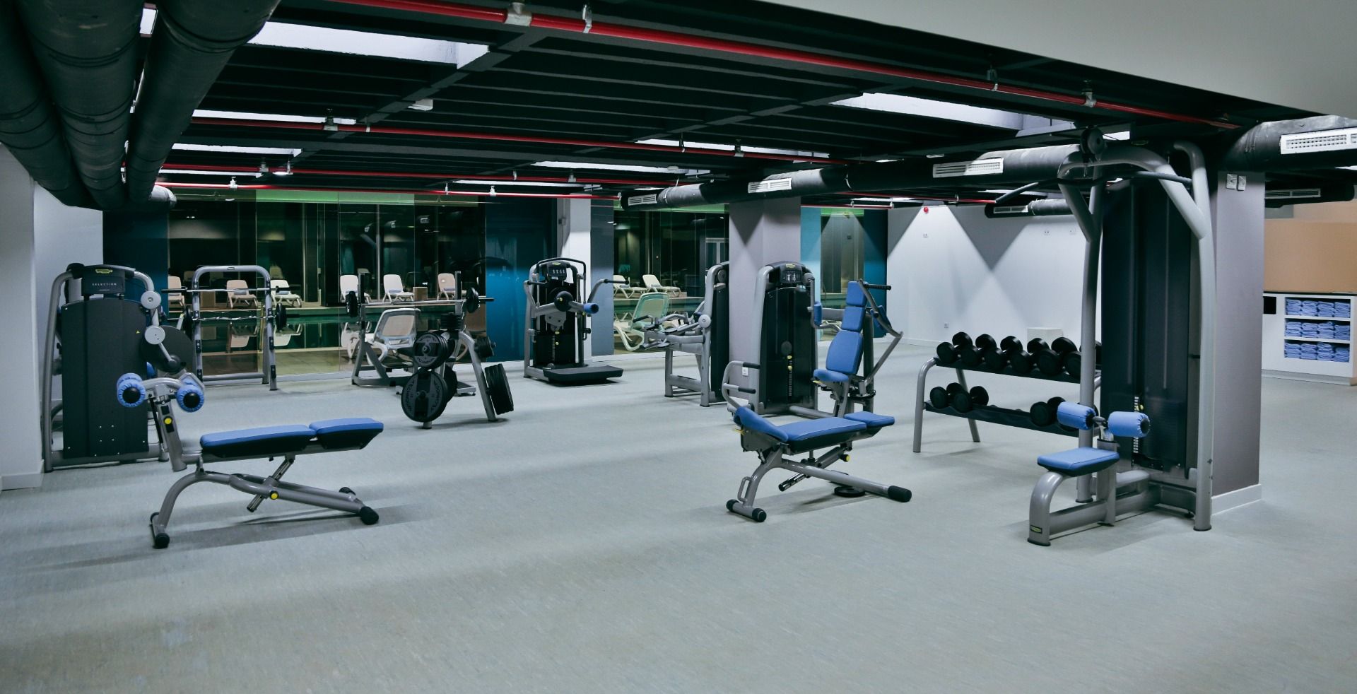 Gut ausgestatteter Fitnessraum mit modernen Geräten, darunter Hanteln, Laufbänder und Krafttrainingsmaschinen