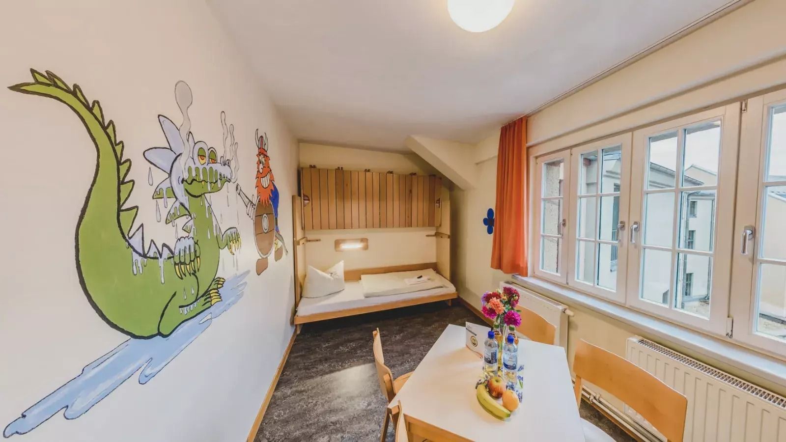 Großzügiges Zimmer mit Einzelbett, Tisch mit Stühlen und einer kindlichen Wandmalerei mit Drache und Wikinger