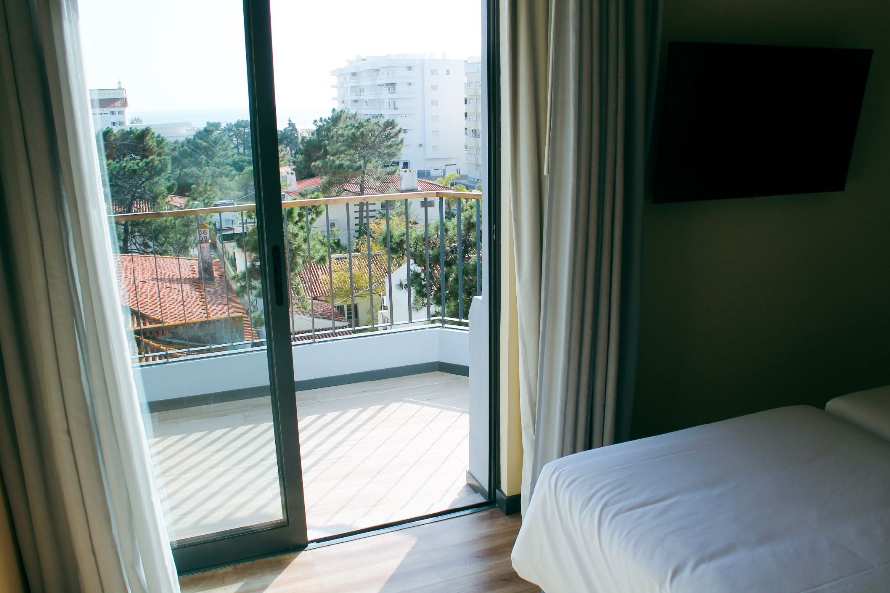 Blick aus einem Hotelzimmer auf einen Balkon und die umliegende Landschaft mit Gebäuden und Bäumen.