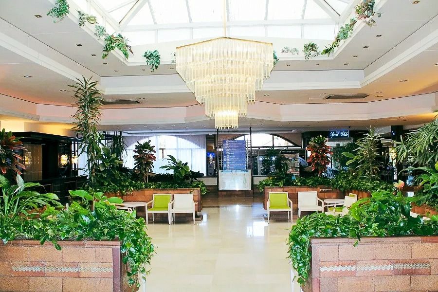Elegante Hotellobby mit Glasdach, großer Kronleuchter, üppiger Bepflanzung und gemütlichen Sitzbereichen.