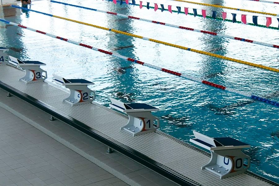 Blick auf Startblöcke und Bahnenmarkierungen eines Wettkampf-Schwimmbeckens mit klarem Wasser.