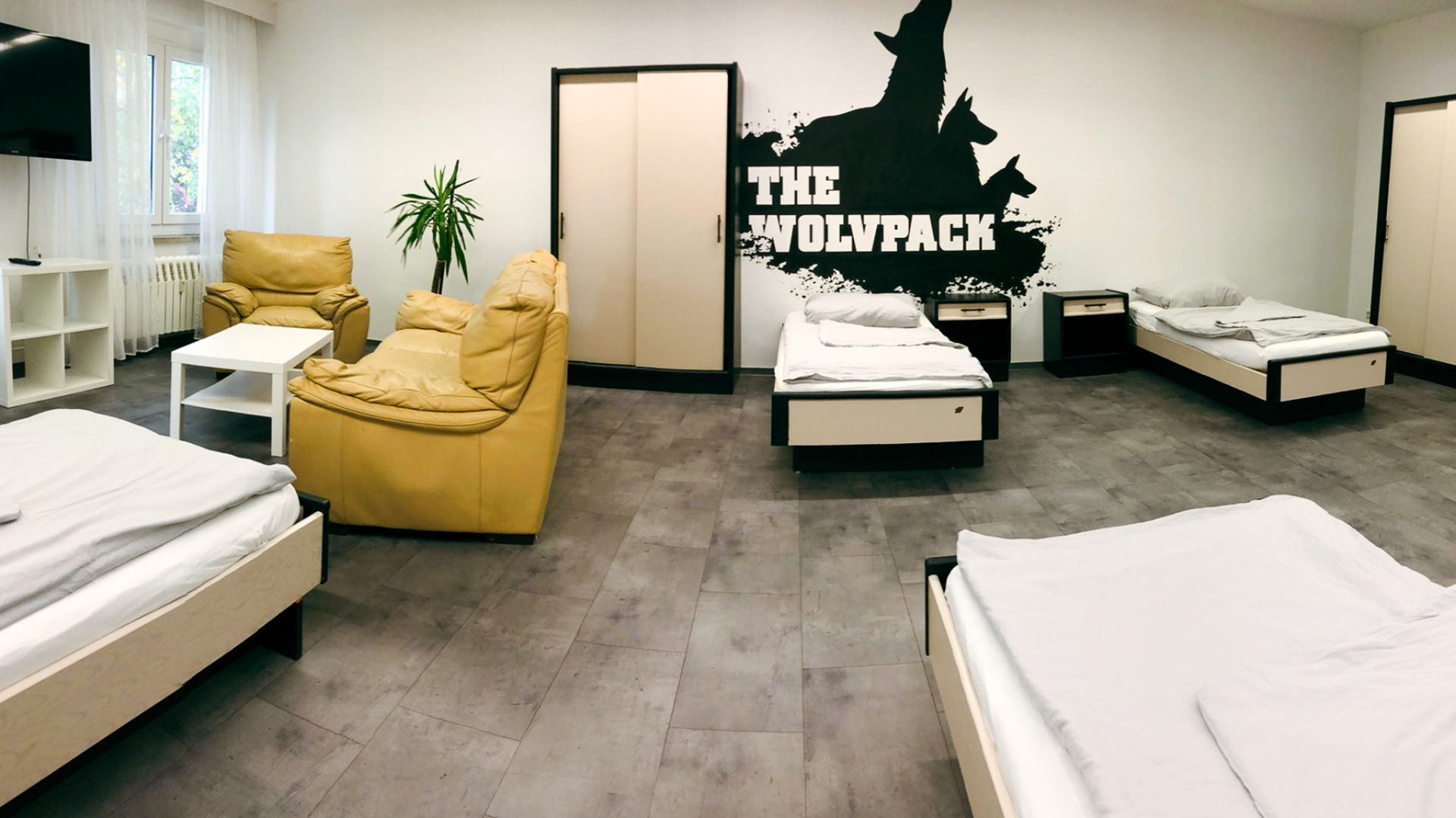 Gemütlicher Schlafraum im Sportcampus Schlotheim mit mehreren Betten, Sitzbereich mit Ledersesseln und Wandgestaltung mit 'The Wolfpack' Motiv