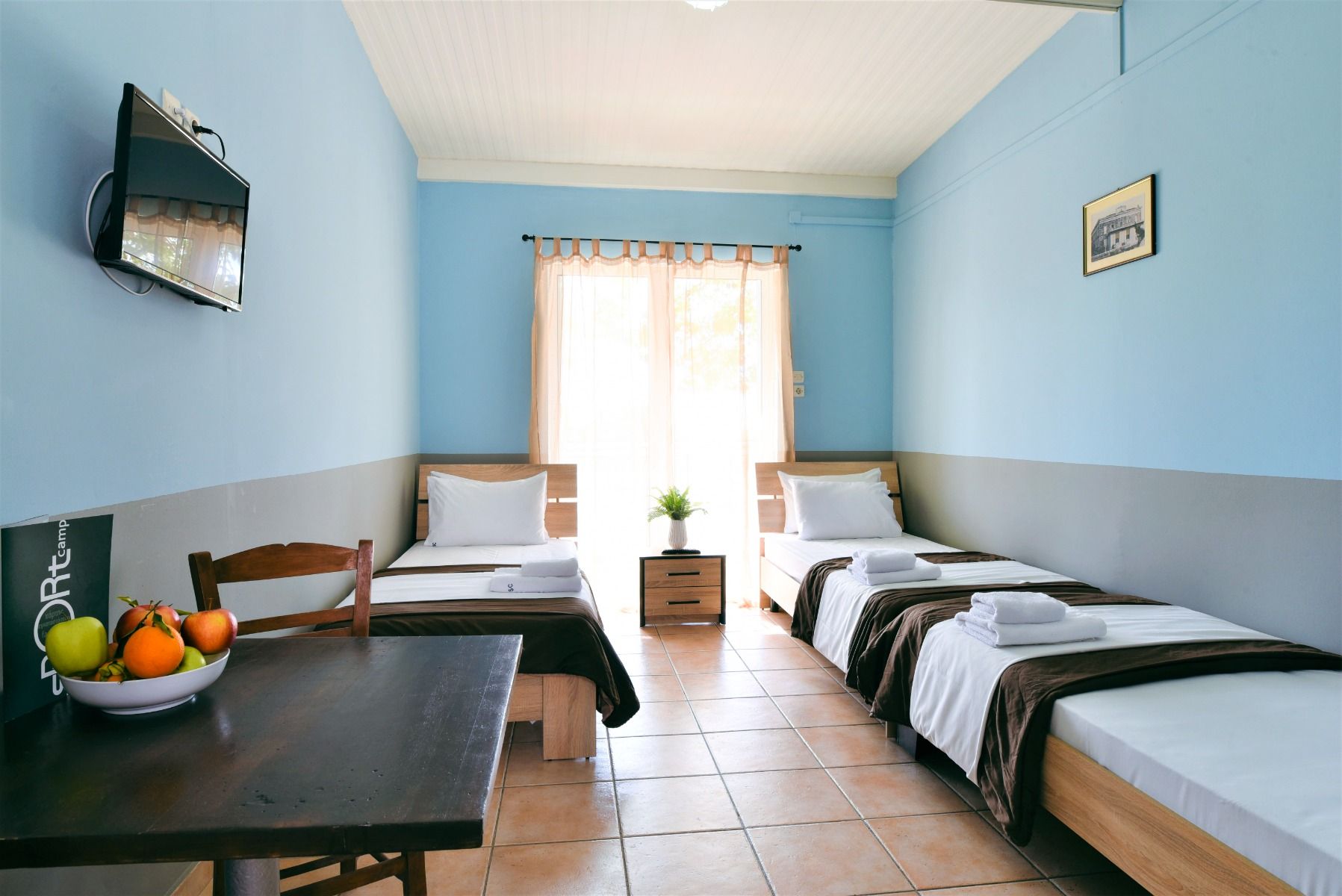 Helles und freundliches Dreibettzimmer mit Einzelbetten, großem Fenster, Fernseher und Tisch im Sport Camp Loutraki