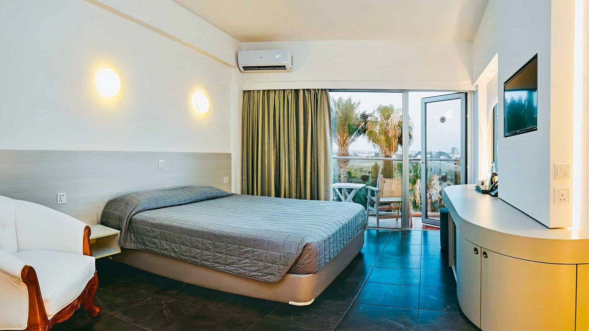 Helles Hotelzimmer im Sveltos Hotel mit Doppelbett, Balkon, Sitzbereich und Blick auf Palmen und Umgebung.