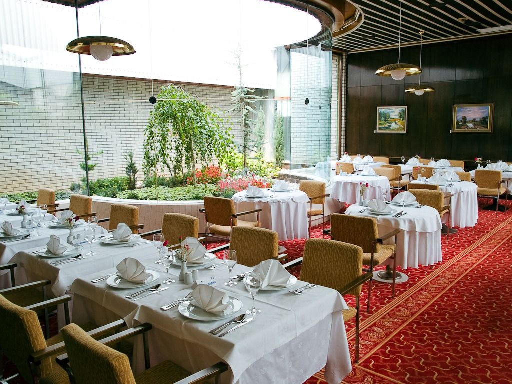 Ein stilvoll eingerichtetes Restaurant mit weiß gedeckten Tischen, rotem Teppichboden und einem bepflanzten Innenhof.
