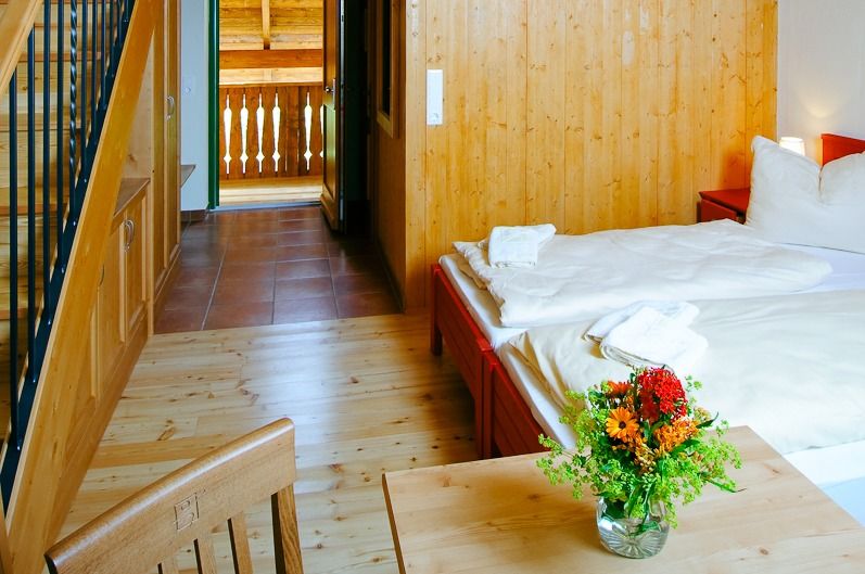 Helles Hotelzimmer mit Holzmöbeln, frischen Blumen auf dem Tisch und einer Treppe, die zu einem Loftbereich führt.