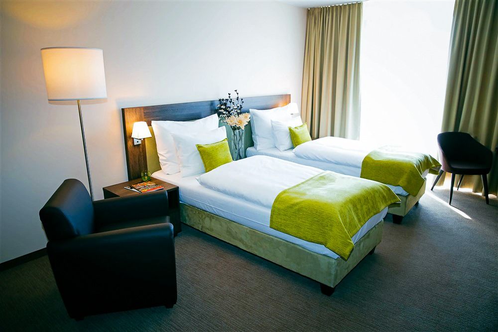 Modernes Hotelzimmer mit zwei Einzelbetten, grünen Akzenten, einem Sessel und einer Stehlampe im X-Bionic Sphere Hotel.