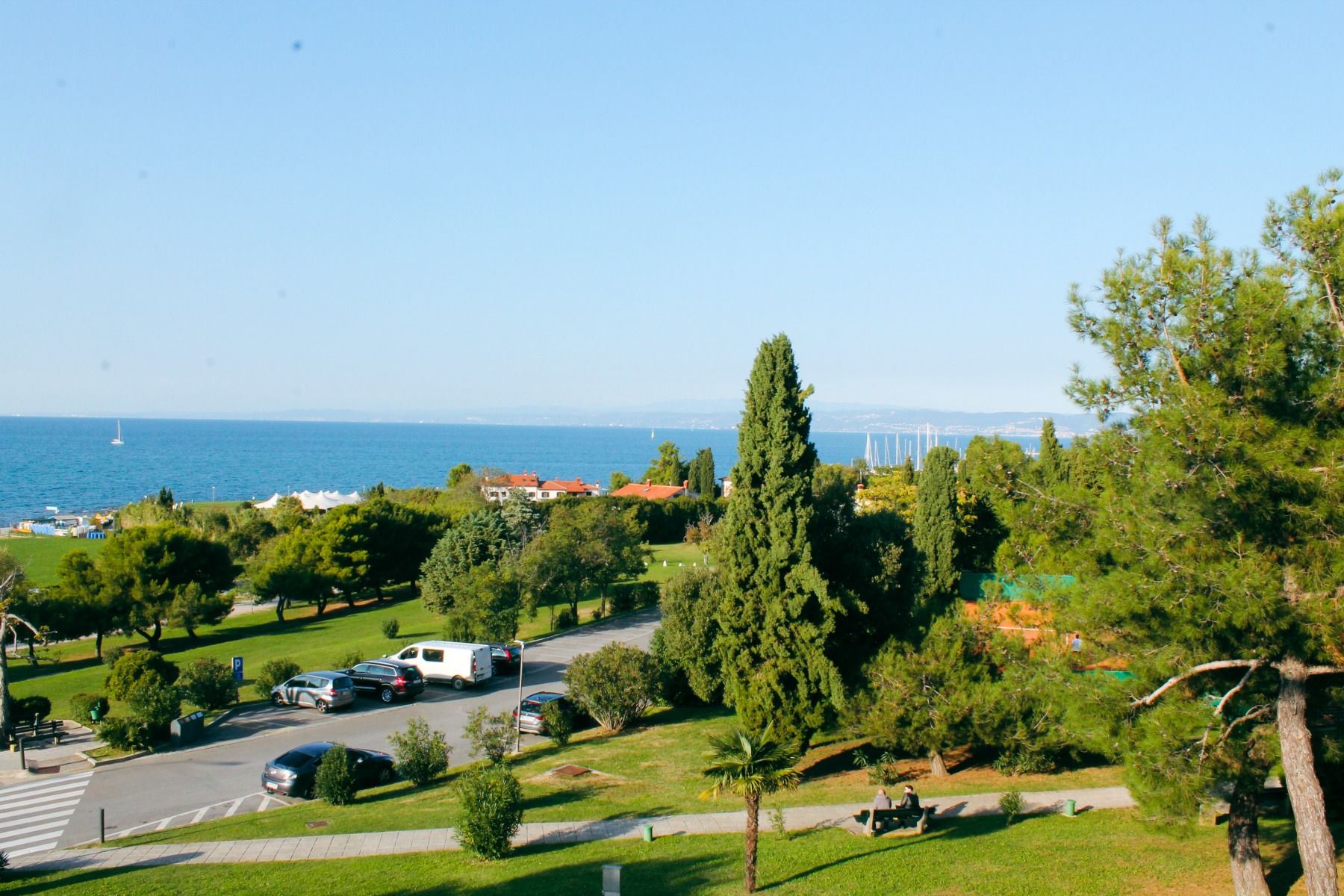 Meerblick vom Hotel San Simon Dependance mit Bäumen, Parkplatz und Küstenlinie.